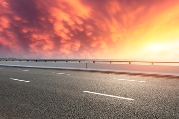 Asphalt road and dramatic sky with coastline at sunset
