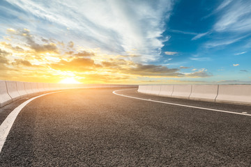 Asphalt road and dramatic sky with coastline at sunset