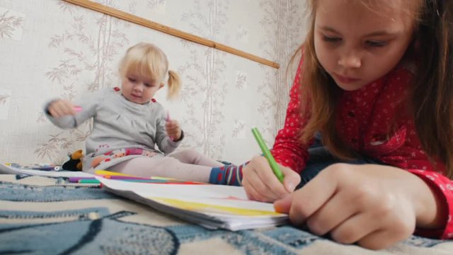 Two little girls lying on the bed and drawing