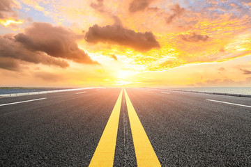 Asphalt road and dramatic sky with coastline at sunset