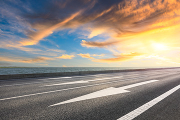 Asphalt road and dramatic sky with coastline at sunset