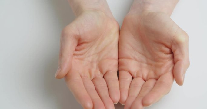 Top view shot of empty female hands opening over a white surface.