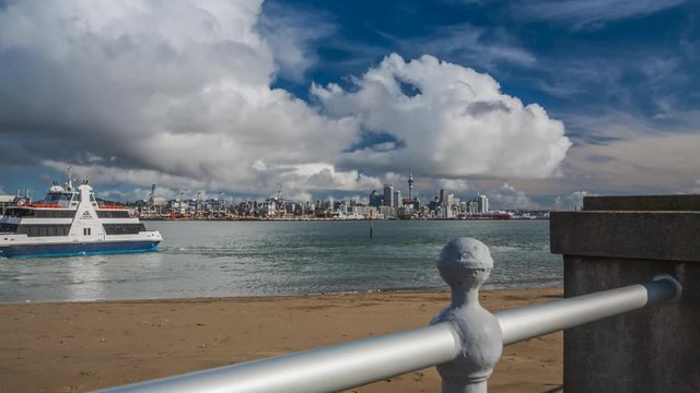 Timelapse of Auckland, New Zealand from Devonport with the ferry coming and leaving. Cityscape of the city centre on the other bank below dramatic clouds.
