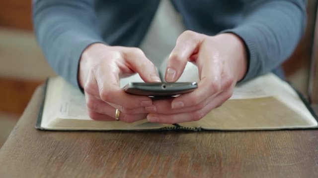 Young Christian woman typing on a mobile phone while studying the Bible. Camera pan to the right.