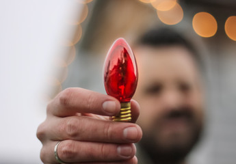 man holding up an old fashioned red Christmas light bulb