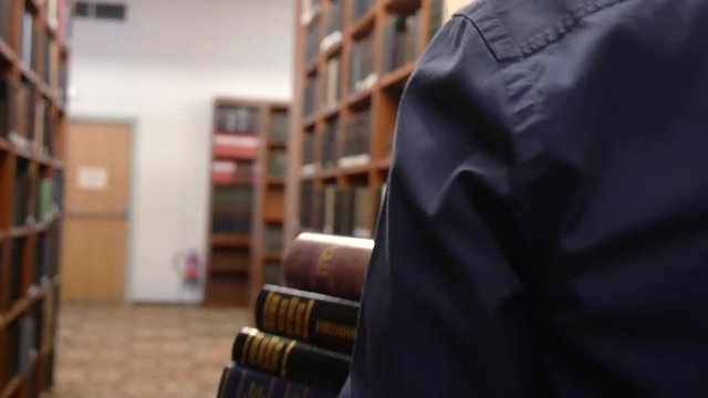 Over the shoulder tracking shot following a man carrying a stack of books through a library