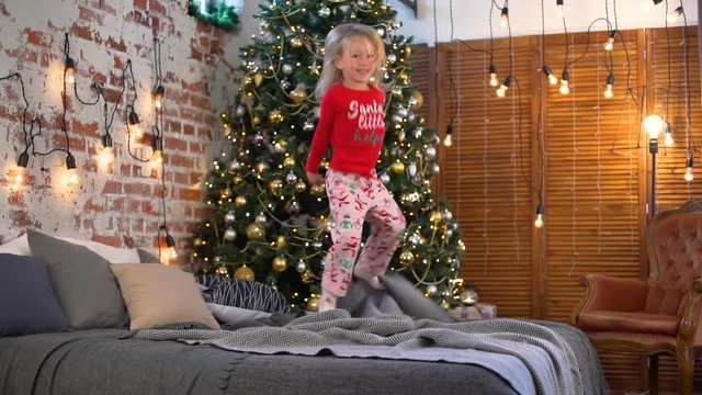 Little Girl Jumping on the Bed near the Christmas Tree