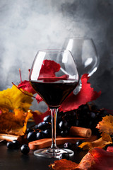 Dry red wine in large glass, autumn still life with red and yellow leaves on gray background, wine...