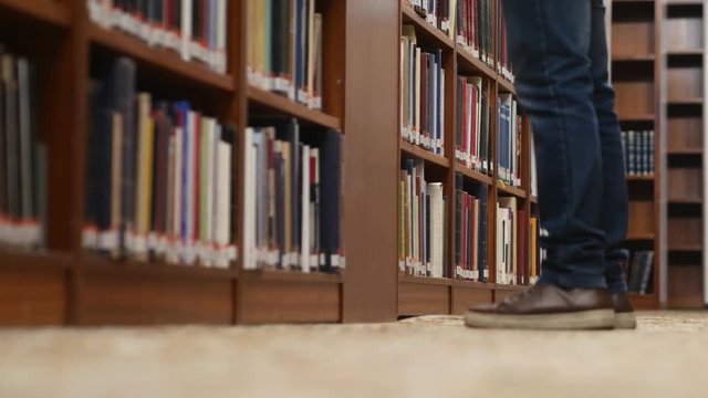 Low angle shot of a person's legs walking as they stop to look for a book in the library