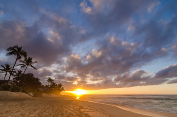 Sun setting over waves on the beach and a vast sky on Sunset Beach on the north shore of Oahu,...