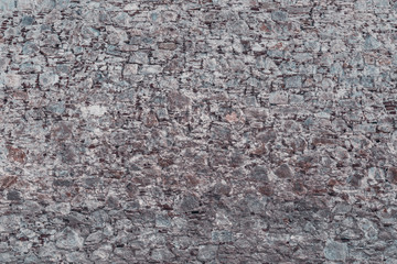 Wide-angle shot of the texture of the wall where broken bricks mixed with stones of different sizes, concrete, and cement layers
