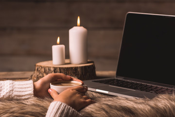 white cup with coffee in the hands of a girl, computer, fur and candles 