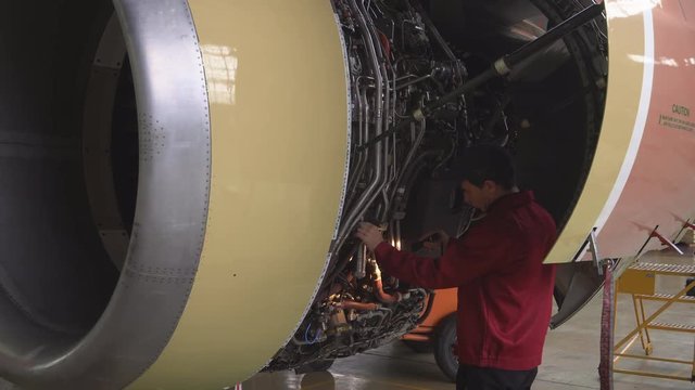 Engineer, technician examines the jet engine with a flashlight. The repair of aircraft in the hangar. Maintenance of aircraft. 4k