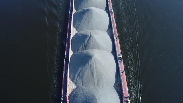 Aerial view. The barge floats on a wide river loaded with rubble. The bulk carrier transports gravel on a navigable river. Vertically view of dry cargo ship from drone.