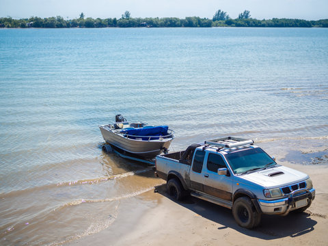 Motor boat being pulled with the pickup truck trailer on the beach