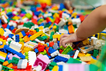 Close up baby child hand catching or selecting the colorful plastic several size toy brick blocks in the tray.