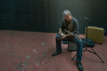 Asian attractive older homeless street musician relaxes his body on electric amplifier after...