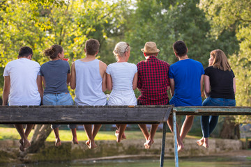 rear view of friends enjoying watermelon while sitting on the wooden bridge