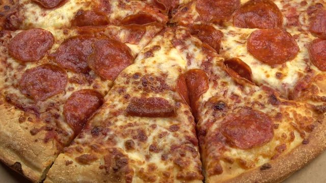 Edge of sliced whole pepperoni pizza spinning video close up