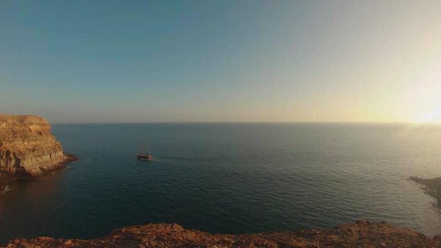 Sunset in Tirita&radic;&plusmn;a Beach, Gran Canaria, Spain, with a boat sailing and blue sky framed by high cliffs near Taurito/Mogas, between Punta de la Cruz de Piedra and Punta de los Medios Almudes.