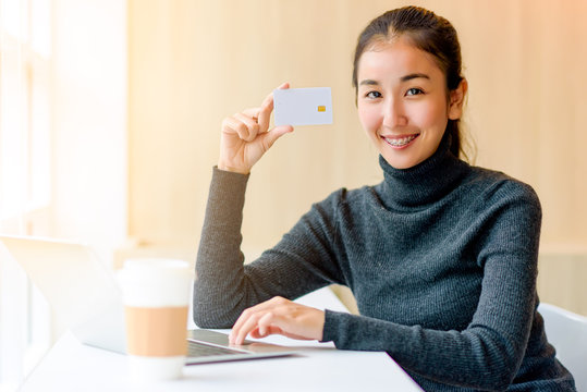 Asian attractive happy smart smile business woman holding credit card and use laptop for shopping online on e-commerce website in the morning time with a cup of coffee. © livertoon
