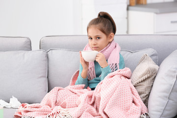Little girl with cup of tea for cough on sofa at home