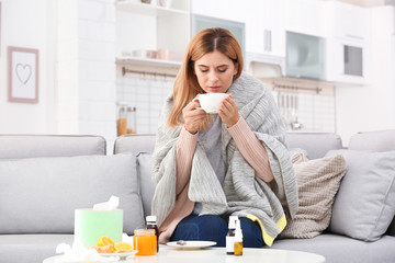 Woman with cup of tea for cough on sofa at home