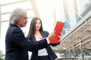 Asian smart old manager boss point on his secretary noteboard for tell her about the company project and his schedules and appointments at skywalk on metro station in center business zone of city.