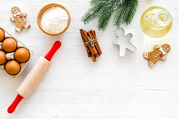 Fototapeta na wymiar Ingredients for New Year gingerbread cookies. Eggs, flour, cinnamon, oil near gingerbread man, rolling pin and spruce branch on white background top view space for text
