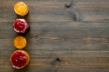 Set of sweet jams in glass jars on dark wooden background top view space for text