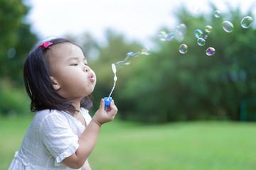 Asian cute little girl blowing to make many bubbles in public garden at holiday or vacation. Playtime Concept.
