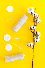 Cotton hygiene products. Cotton pads and swabs, towels twisted coil near dry cotton flowers on yellow background top view