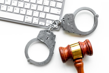 Arrest of a hacker for cyber fraud concept. Handcuff near keyboard and judge gavel on white...