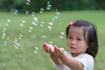 Bubbles in front of the blur of asian cute little girl. she tries to touch bubbles with her hands in public garden. Playtime Concept.