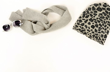 Women clothes and accessories set on white background top view. Stylish autumn and winter concept grey scarf, knitted hat, sunglasses