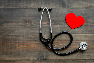 Health care concept. Stethoscope near heart sign on dark wooden background top view copy space