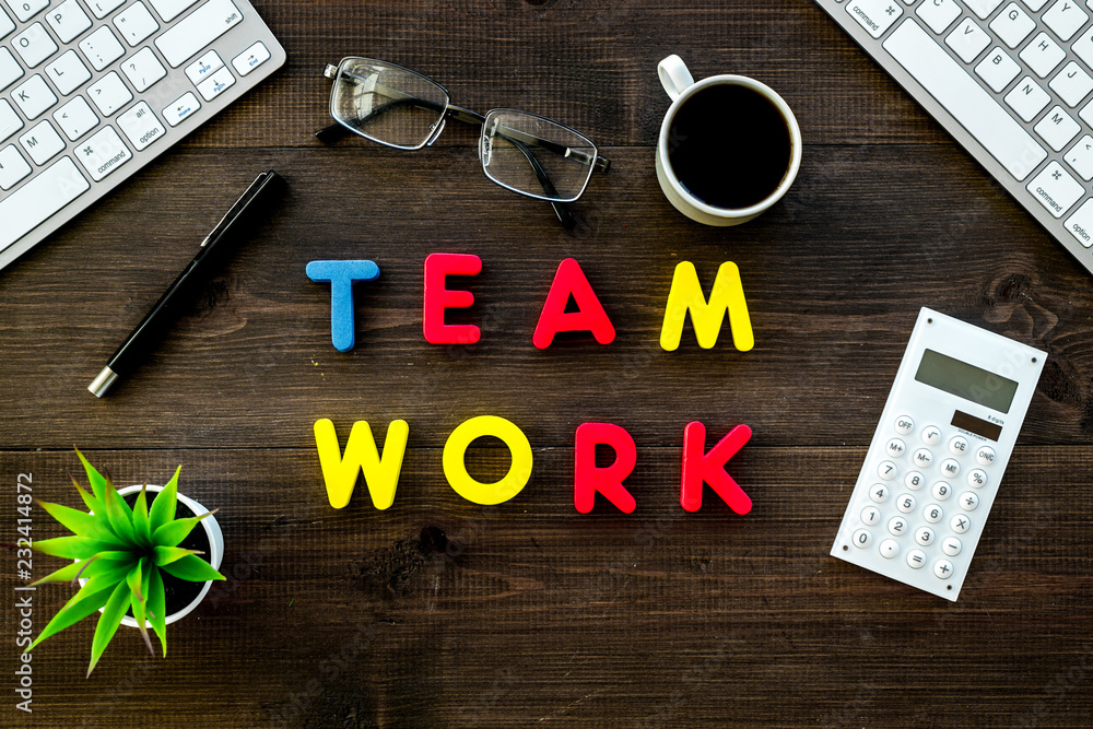 Poster teamwork in office. text teamwork lined with colored letters on dark wooden office desk with compute