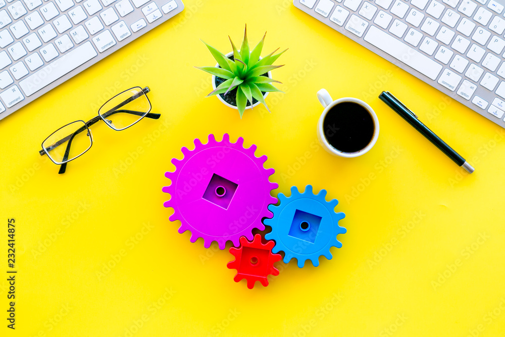 Poster teamwork in business concept. toy gears on yellow office desk with computer keyboard top view copy s