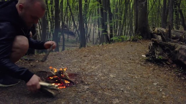 Man making firecamp in the forest. Male firewood Campfire alone outdoor In the woods. Hiker resting after trekking and starting bonfire