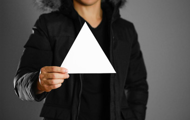 A man in a warm winter jacket holds a triangular white leaflet. Blank paper. Close up. Isolated background