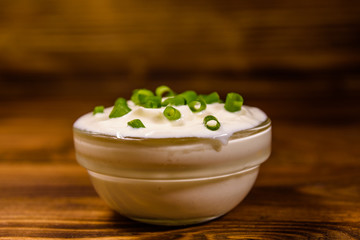 Fototapeta na wymiar Glass bowl with sour cream and chopped green onion on wooden table