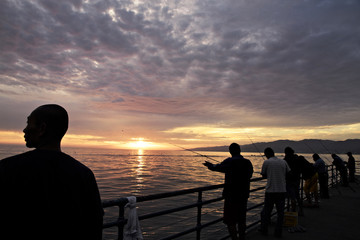 Silhouetted fishermen on Venice Pier at sunset, California