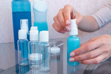Woman's hands twist cap on a small bottle of shower gel. Travel set of jars.
