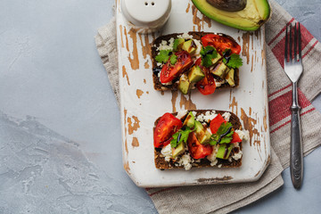 Avocados, cherry tomatoes and feta cheese sandwiches with balsamic sauce and cilantro on old olive board. Top view.