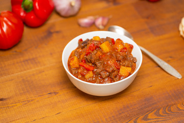 Meat stew with beef, potato, carrot, onion, spices,tomato and pepper . Slow cooked meat stew, bowl, wooden background. Hot autumn-winter dish. Close up.