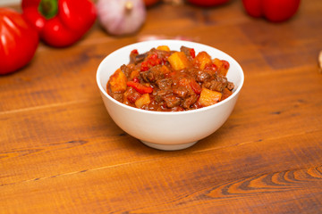 Meat stew with beef, potato, carrot, onion, spices,tomato and pepper . Slow cooked meat stew, bowl, wooden background. Hot autumn-winter dish. Close up.
