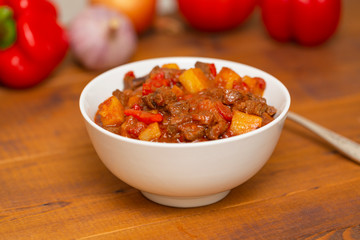 Meat stew with beef, potato, carrot, onion, spices,tomato and pepper . Slow cooked meat stew, bowl, wooden background. Hot autumn-winter dish. Close up.