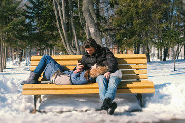 Woman sleeps, man look at phone. Man and a woman rest together on a bench in the winter city Park....