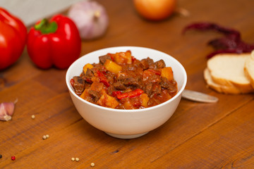 Meat stew with beef, potato, carrot, onion, spices,tomato and pepper . Slow cooked meat stew, bowl, wooden background. Hot autumn-winter dish. Close up.