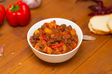 Meat stew with beef, potato, carrot, onion, spices,tomato and pepper . Slow cooked meat stew, bowl, wooden background. Hot autumn-winter dish. Close up.